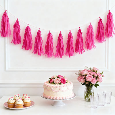 Pink tassel garland with cake, cupcakes, and flowers for a festive celebration.