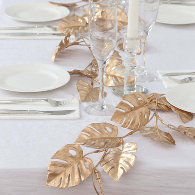 Gold leaf table runner with elegant glassware and plates on a white tablecloth.