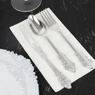 Elegant silverware set on a decorative napkin beside a fine china plate.