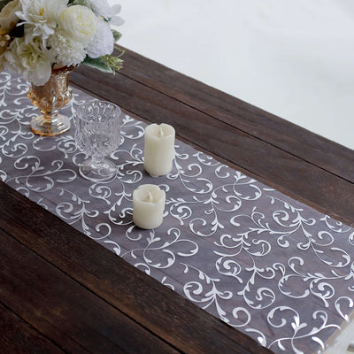 Elegant silver leaf table runner on rustic wooden table with candles and flowers.