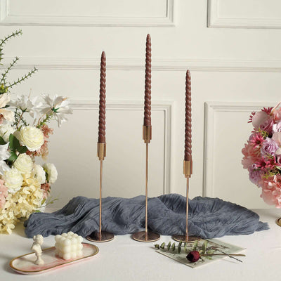 Bronze candle holders with twisted brown candles and floral decor on a table.