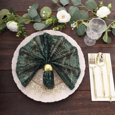 Elegant green sequin napkin folded on a decorative plate with cutlery and floral accents.