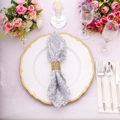 Elegant silver napkin with a decorative ring on a white plate, surrounded by floral arrangements.