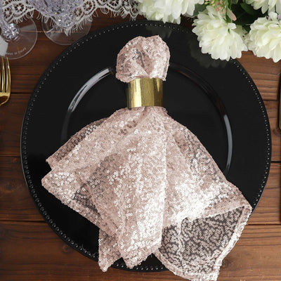 Rose gold sequin napkin on a black plate with floral decor in the background.