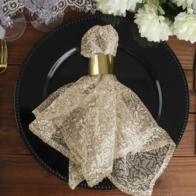 Gold sequin napkin with a gold ring on a black plate.