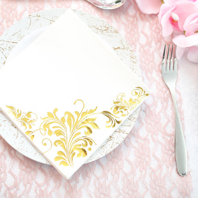 White napkin with gold floral design on a decorative plate.