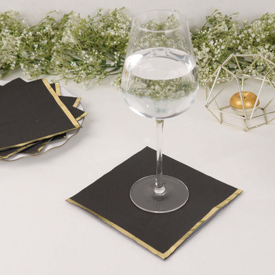 Black napkin with gold trim under a wine glass on a neutral table setting.