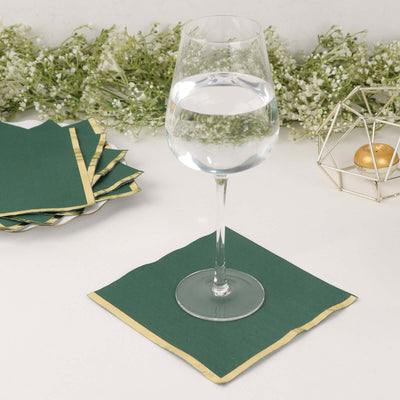 Green napkin with gold trim under a wine glass on a clean surface.