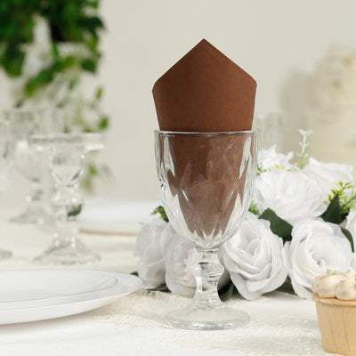 Brown paper napkin in a glass on a dinner table with floral decor.