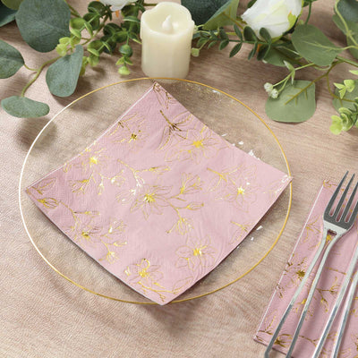 Pink floral napkin on a clear plate with cutlery and decorative greenery.