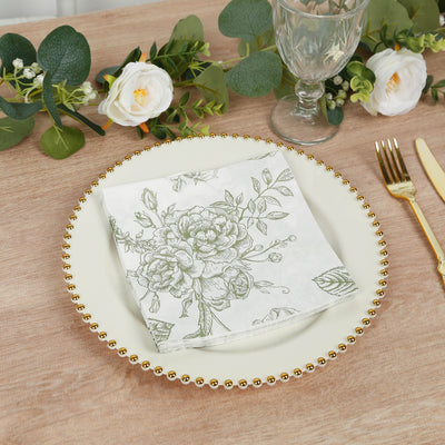 Floral-patterned napkin on a decorative plate with greenery and glassware around it.