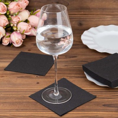 Elegant wine glass with water on a black coaster, surrounded by roses and plates.