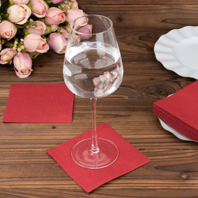 Water glass on red napkin with bouquet and plate on wooden table.