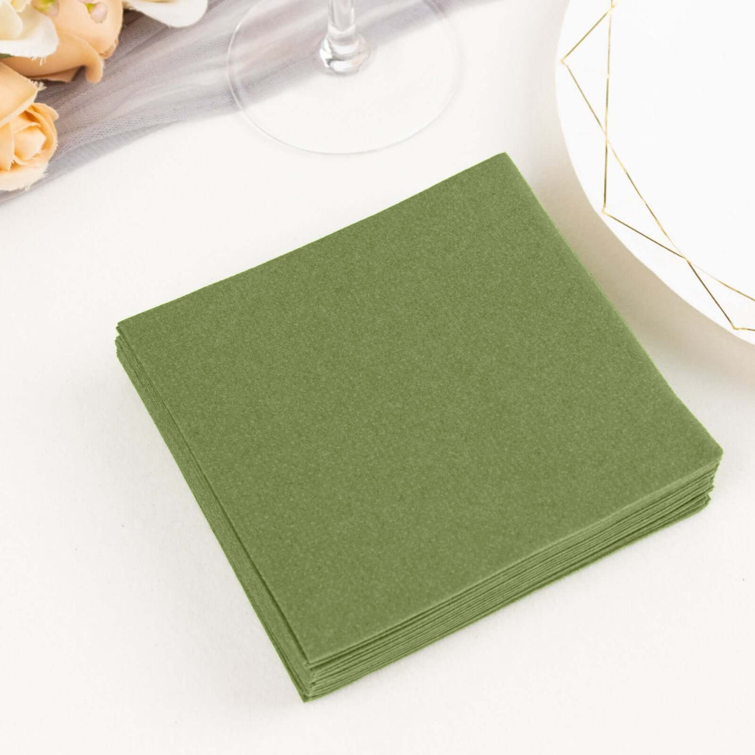 Green paper napkins stacked on a table with floral accents.