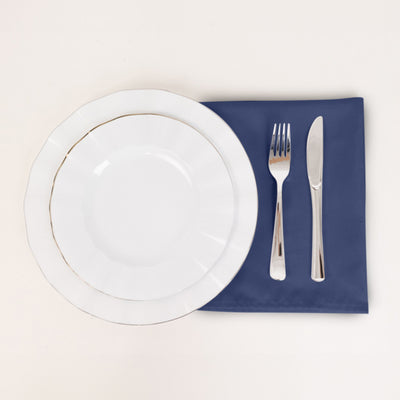 Elegant white dinner plate with silver trim, fork, and knife on a navy napkin.