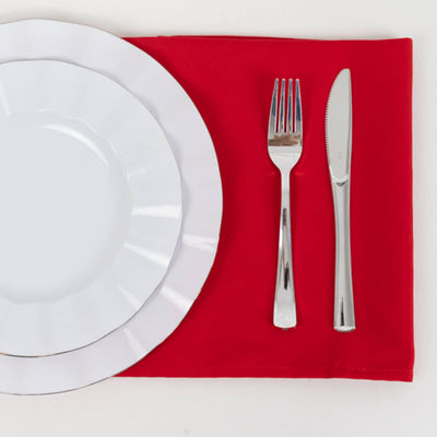 White dinner plates and silverware on a red placemat.