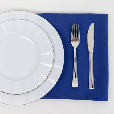 Elegant white dinnerware set with silver trim on a blue napkin.