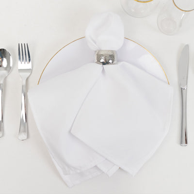 Elegant white napkin on a plate with a silver napkin ring and cutlery.