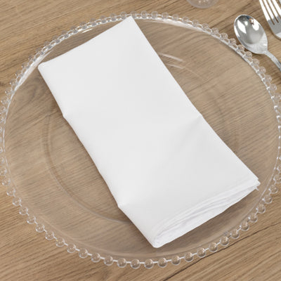 White napkin neatly folded on a clear plate with silverware set.