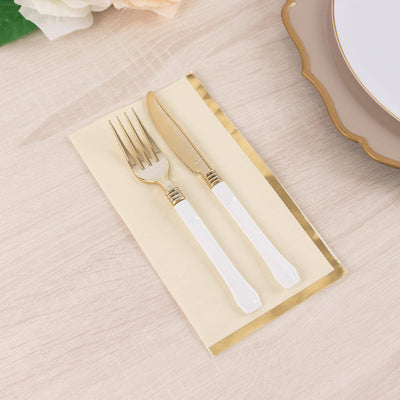 Gold-accented cutlery set with white handles on a beige napkin.