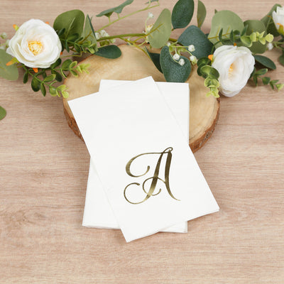 Personalized napkins with gold letter "A" on a wooden slice with greenery and flowers.