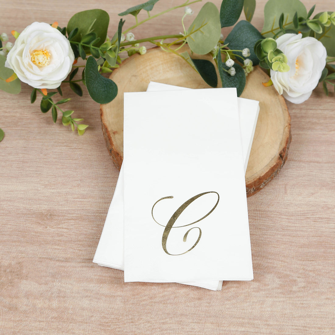 Elegant white napkins with gold monogram "C" on rustic wood background.