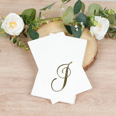 Elegant white napkins with gold letter "J" monogram on a wood slice backdrop.