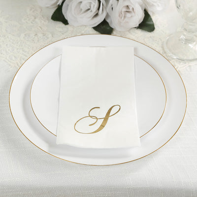 Gold monogram napkin on elegant white plates with floral backdrop.