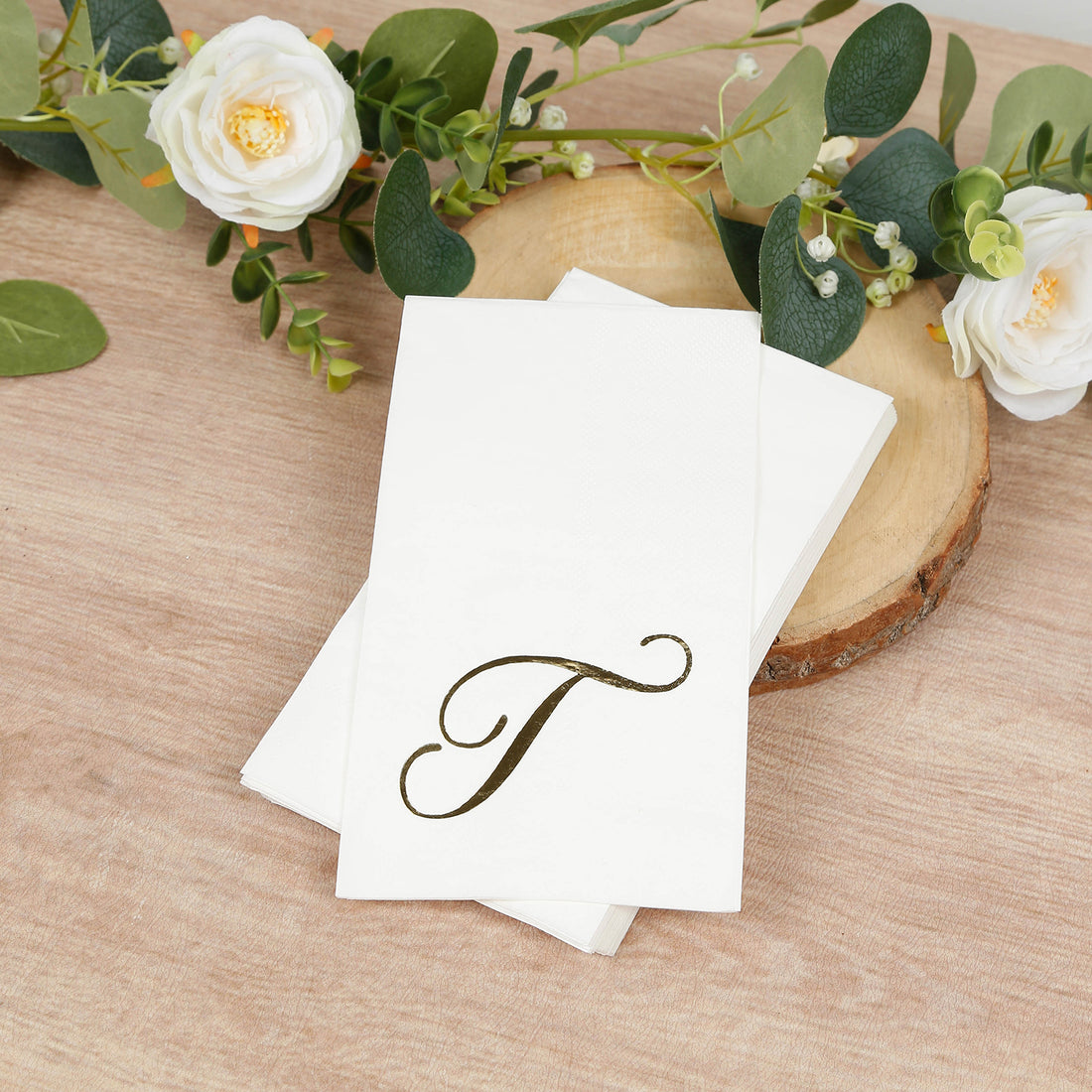 Elegant gold initial "T" on white napkins with floral decor.