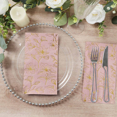 Pink floral napkin on a clear plate with cutlery and greenery accents.
