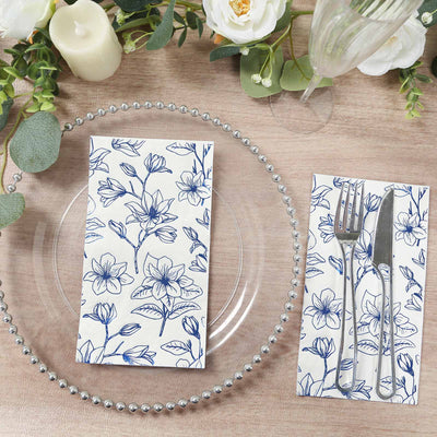 Floral-patterned napkin on a clear plate with cutlery and decor elements.