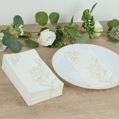 Elegant floral napkins stacked next to a plate and greenery on a table.