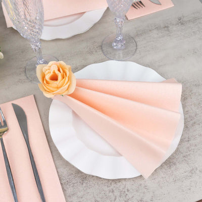 Elegant peach napkins and rose on a white plate for a stylish table setting.