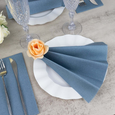 Blue napkin elegantly folded with a rose on a white plate, set on a textured table.