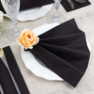 Black napkin elegantly folded with a rose on a white plate at a dining table setting.