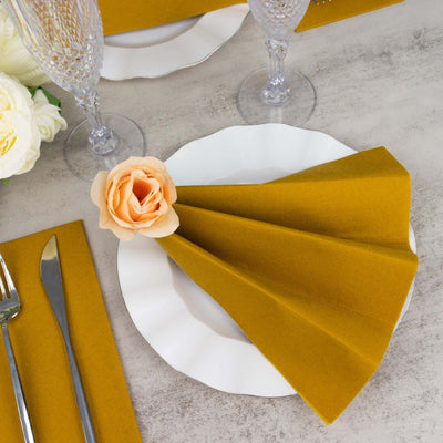 Elegant table setting with mustard napkin and flower accent on a white plate.