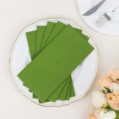 Green paper napkins neatly arranged on an elegant plate with flowers in the background.