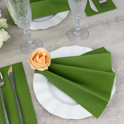 Green napkins elegantly folded on a white plate with a peach rose, set for dining.