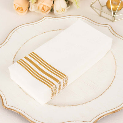 White napkin with gold stripes on decorative plate.