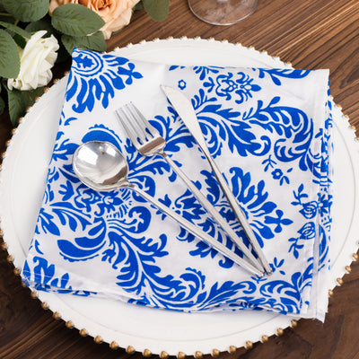 Blue floral napkin with silver cutlery on a textured wooden table.