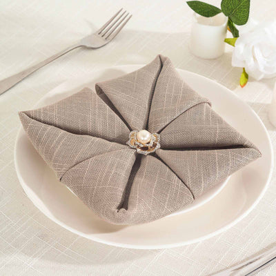 Elegant folded napkin with a pearl brooch on a dinner plate.