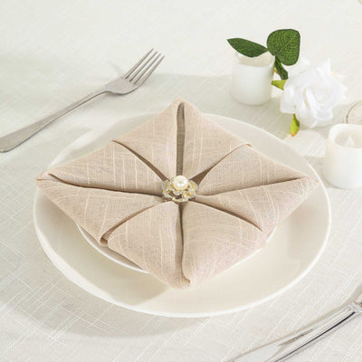 Elegant beige napkin with decorative ring on a white plate.