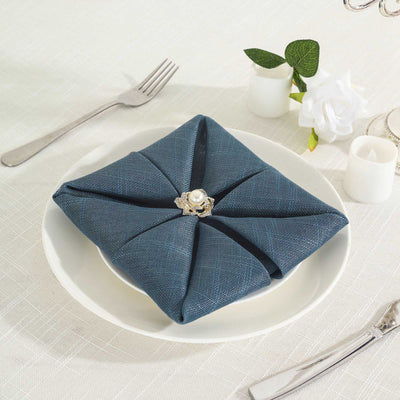 Elegant blue napkin folded with a pearl ring on a white plate.