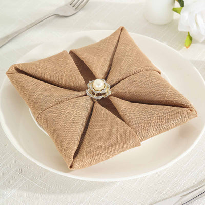 Elegant brown napkin folded with a pearl brooch on a white plate.