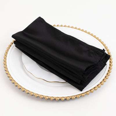 Black satin napkins neatly folded on a decorative plate.