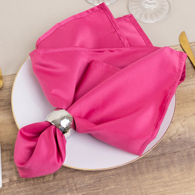 Pink satin napkin elegantly arranged on a white plate with a silver napkin ring.