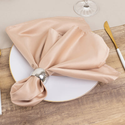 Elegant satin napkin with silver ring on a white plate, set on a wooden table.