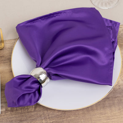 Purple satin napkin elegantly tied with a silver napkin ring on a plate.