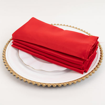 Stack of red satin napkins on a decorative plate.