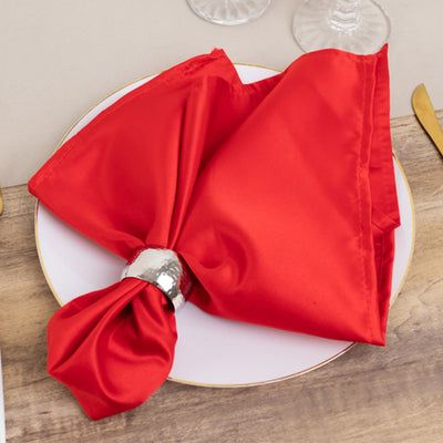 Red satin napkin elegantly tied with a silver ring on a decorative plate.